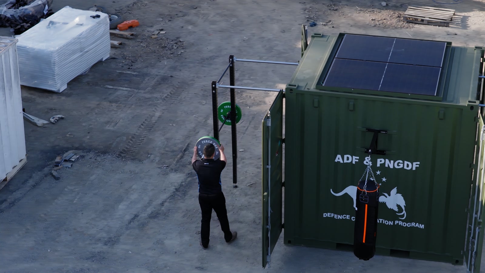 Aerial footage frame of the green Rapid-10 with open doors, exterior rig and rooftop panels at the fabrication yard